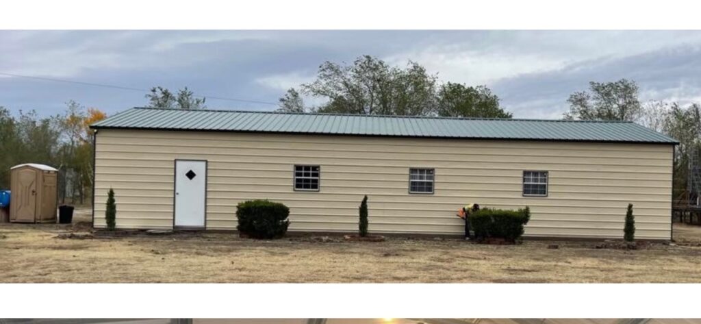 Long tan metal building with green roof, walk door and three windows