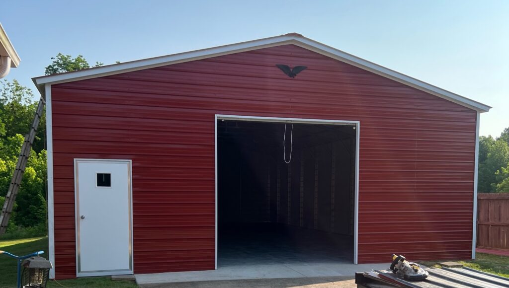 Red metal barn with eagle emblem, open garage door and white trim
