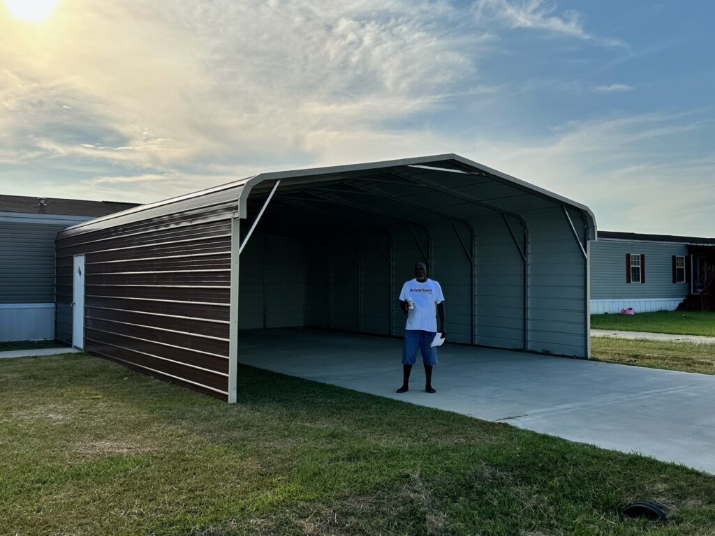 Three-sided metal carport with one enclosed wall and concrete pad