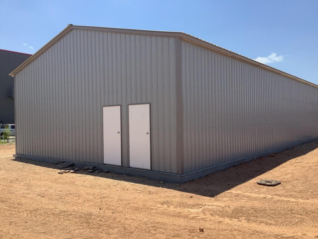 Large tan commercial metal building with two walk doors on a dirt lot
